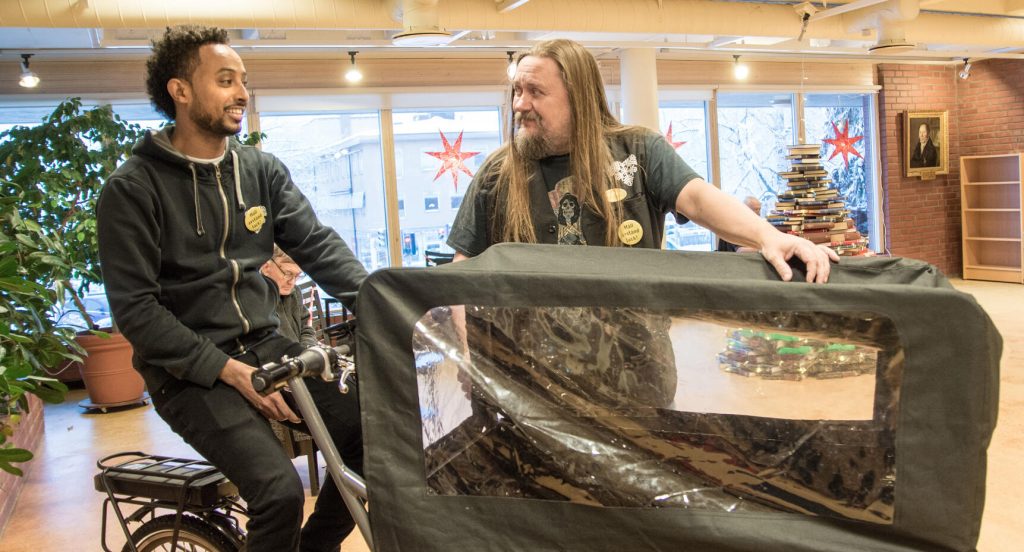 Mhireteab Bhaylzghi kör ut böcker med cykelkärra. Till höger biblioteksassistenten Petri Liljeroos.