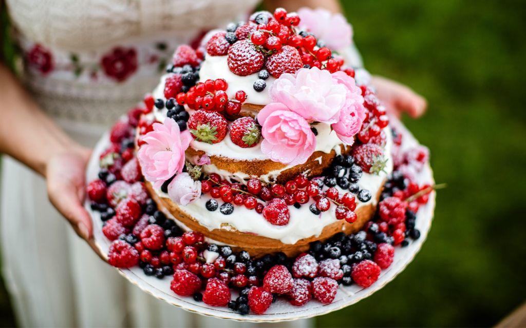 Kvinna håller i tårta med bär som hallon, jordgubbar, blåbär, vinbär, blåbär.